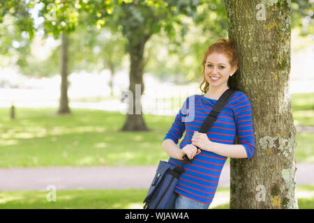 Smiling redhead student leaning against a tree Stock Photo