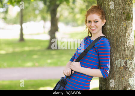 Cute redhead student leaning against a tree Stock Photo