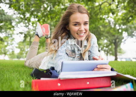 Smiling student lying on the grass studying with her tablet pc Stock Photo
