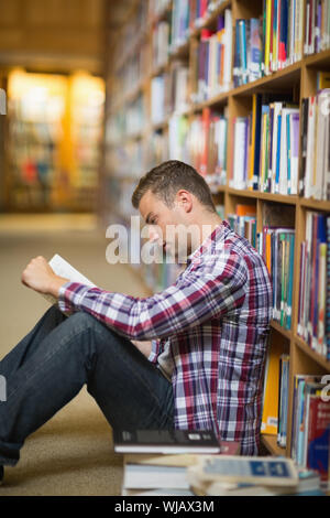 Focused student sitting on library floor reading Stock Photo