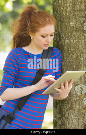 Cheerful student leaning against a tree using her tablet Stock Photo