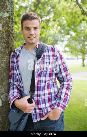 Handsome student leaning on tree looking at camera Stock Photo