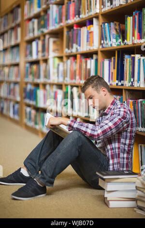 Serious student sitting on library floor reading Stock Photo