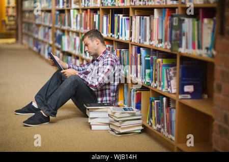 Focused young student sitting on library floor using tablet Stock Photo