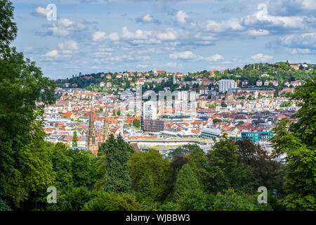 Germany, Downtown stuttgart houses and churches seen from above green tree tops near karlshoehe in summer surrounded by trees and nature landscape Stock Photo
