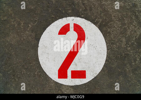 Red number two inside white circle painted on concrete background - top down view, landscape format, copy space Stock Photo