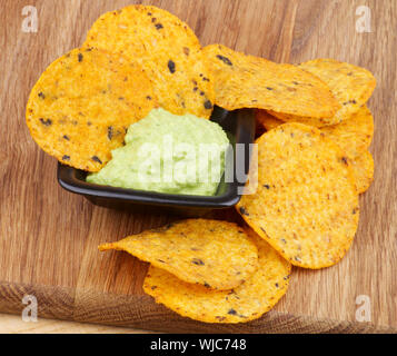 Arrangement of Tortilla Chips and Guacamole Sauce in Black Bowl closeup on Wooden Board Stock Photo