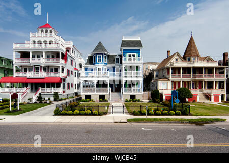 Colorful Victorian style houses alongside a road. Beautiful wooden homes with balconies and porches, painted red, blue, white and orange, under a blue Stock Photo