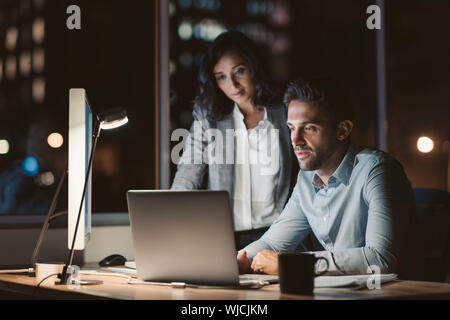 Businesspeople working together on a laptop late in the evening Stock Photo