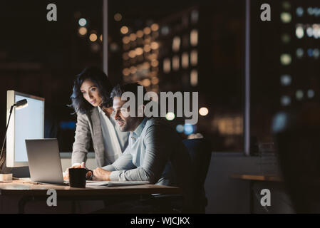 Two work colleagues using a laptop late in the evening Stock Photo
