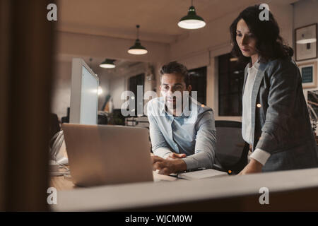 Two young colleagues working late in an office together Stock Photo