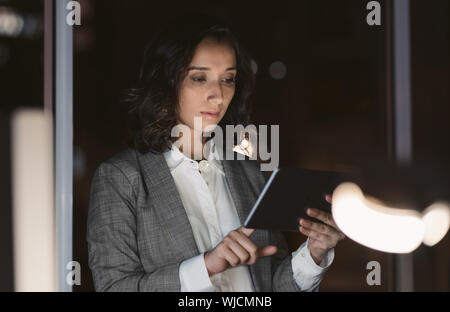 Young businesswoman using her tablet in a dark office Stock Photo