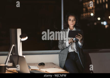 Young businesswoman standing in a dark office using her tablet Stock Photo