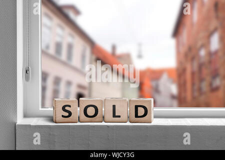 Sold word made with cubes in a window in a city with a view to buildings Stock Photo