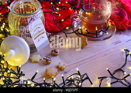 Christmas background. Christmas decoration on wooden table. With lights, cookies, cup of tea, sparkles,... Horizontal photo. Stock Photo