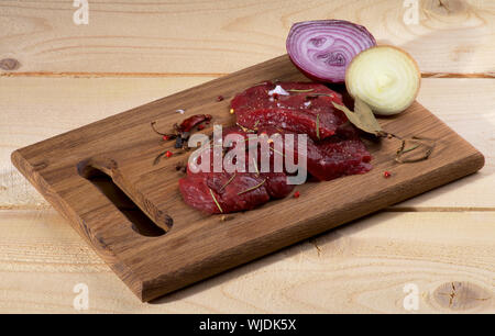 Arrangement of Raw Sliced Beef with Halves of White and Red Onion, Bay Leafs and Spices on Cutting Board isolated on Wooden background Stock Photo