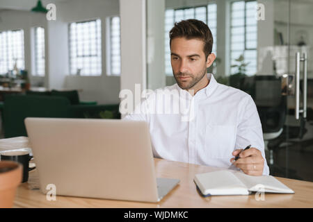 Young businessman writing down notes while working on a laptop Stock Photo