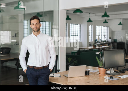 Smiling businessman standing alone in a large modern office Stock Photo