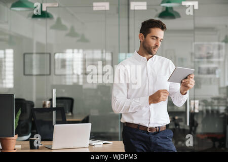Young businessman standing in an office using a digital tablet Stock Photo
