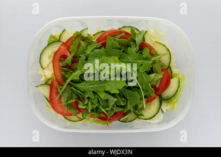 Homemade layered salad in plastic bowl with tomatoes cucumber rocket leaves iceberg lettuce from above Stock Photo