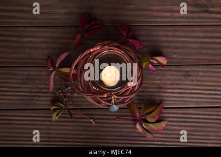 Burning candle in the brown candlestick-basket on the floor. Autumn mood. Stock Photo