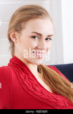 Beautiful caucasian woman sitting ona couch and wearing red pullover. Indoor background. Stock Photo