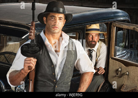 Cute 1920s gangster with submachine gun and partner in car Stock Photo