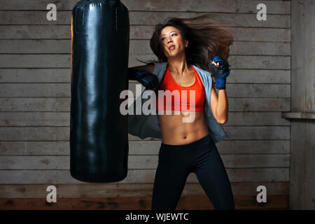 Tough young woman punching boxing bag. Stock Photo