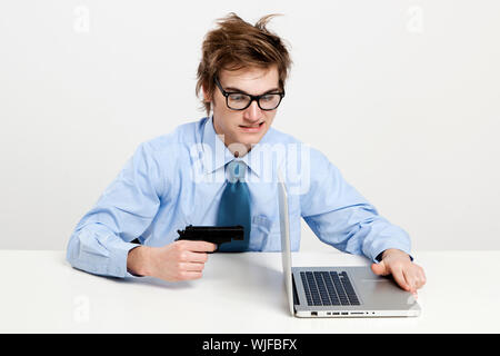 Young man in the office and pointing a gun to the laptop Stock Photo