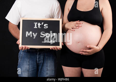Dad holding a chalkboard with the words "It's my Son" and pointing to mom's belly Stock Photo