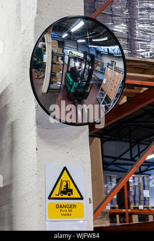 Safety mirror showing a reflection of a fork-lift truck in a warehouse with a 'danger fork-lift trucks' sign beneath (Portrait) Stock Photo