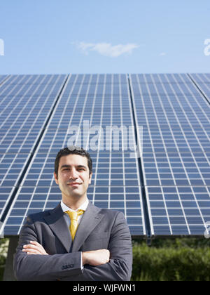 Portrait of mid adult italian male engineer with arms folded in solar power station, smiling at camera. Vertical shape, front view. Copy space Stock Photo