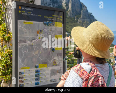 ISLE OF CAPRI, ITALY - AUGUST 2019: Person with sun hat studying a tourist information map in the town of Capri. Stock Photo