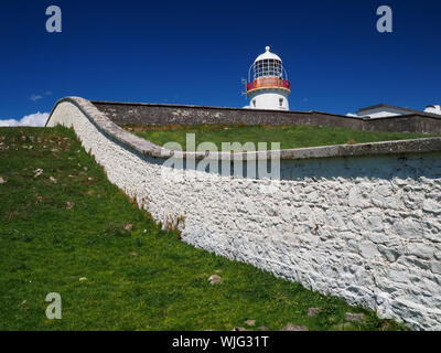 St. John's Point, Co. Donegal, Ireland - May 21st, 2019 - White lighthouse behind white fieldstone wall in front of a clear blue sky Stock Photo