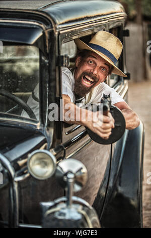 Man in hat and beard shooting gun from old car Stock Photo