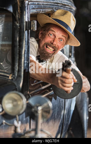 Bearded man firing submachine gun from vintage 1920s car Stock Photo