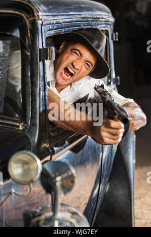 Yelling man firing submachine gun from vintage 1920s car Stock Photo