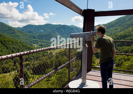 Man looking through telescope on observation deck over forest Stock Photo