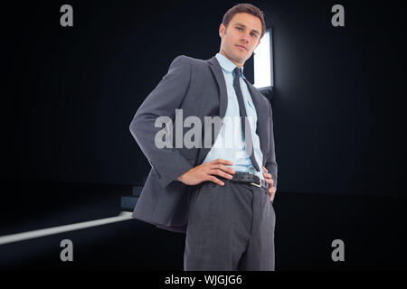 Stern businessman with hands on hips against door opening revealing light at top of steps Stock Photo