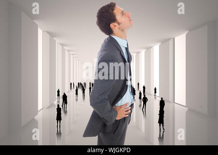 Serious businessman standing with hands on hips against tiny figures in white hall Stock Photo