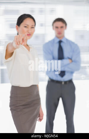 Portrait of a businesswoman pointing towards the camera with man in background at the office Stock Photo