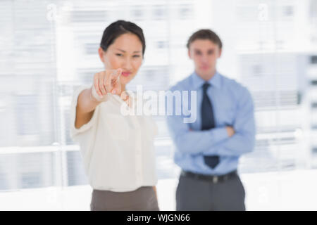 Portrait of a businesswoman pointing towards the camera with man in background at the office Stock Photo