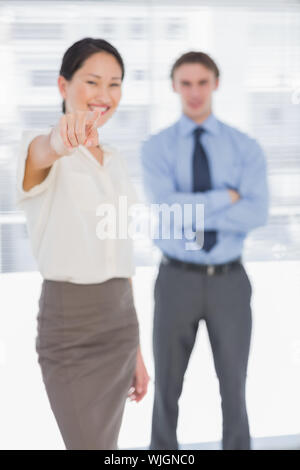 Portrait of a businesswoman pointing towards the camera with man in background at the office Stock Photo