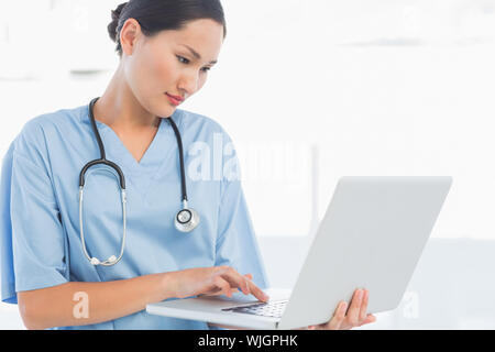 Concentrated female surgeon using a laptop in a bright hospital Stock Photo