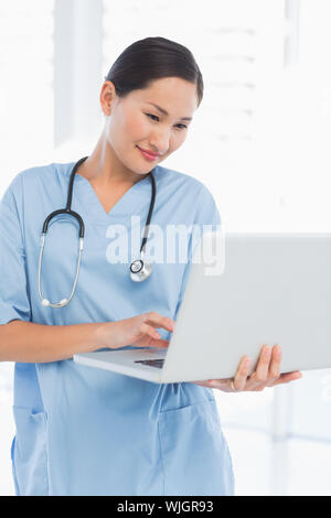 Concentrated female surgeon using a laptop in a bright hospital Stock Photo