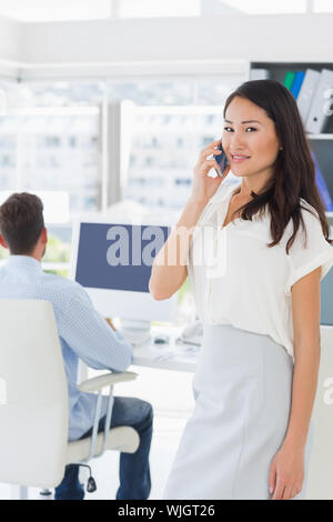 Casual female artist using mobile phone with colleague in the background at a bright office Stock Photo