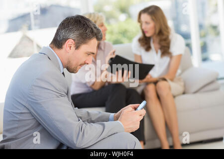 Businessman text messaging with female colleagues sitting on sofa in background at home Stock Photo