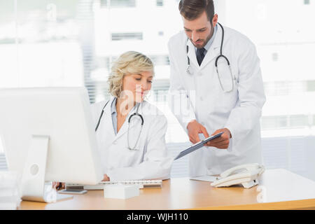 Two doctors using digital tablet by computer at medical office Stock Photo