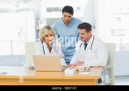 Three concentrated doctors using laptop together at the medical office Stock Photo