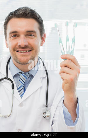 Portrait of a smiling doctor holding toothbrushes in his office Stock Photo